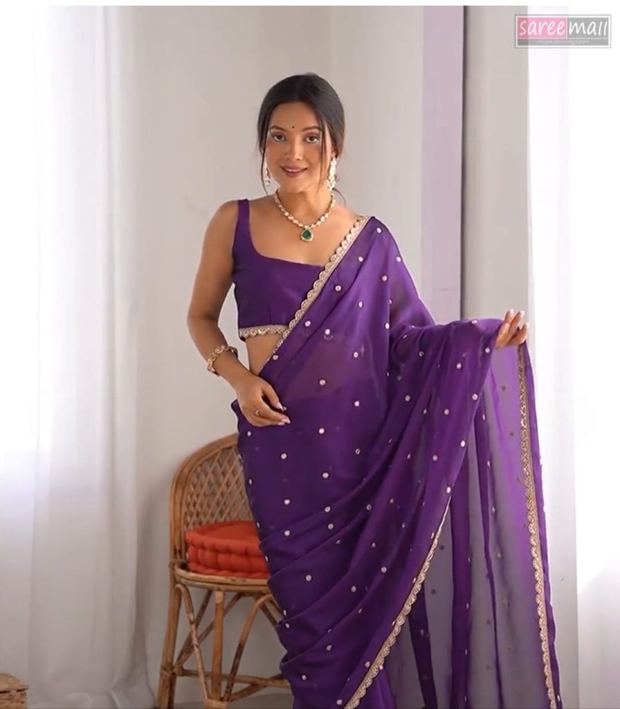 Woman displaying the embellished pallu of a purple georgette saree